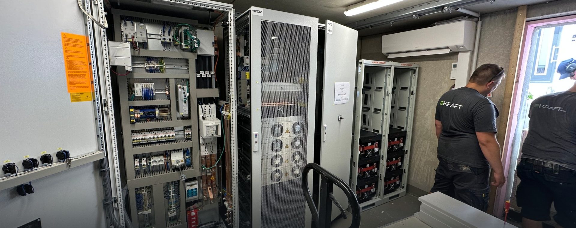 Zwei EKRAFT-Techniker im Speicherraum zwischen Schaltschrank, PCS und Batterie-Racks