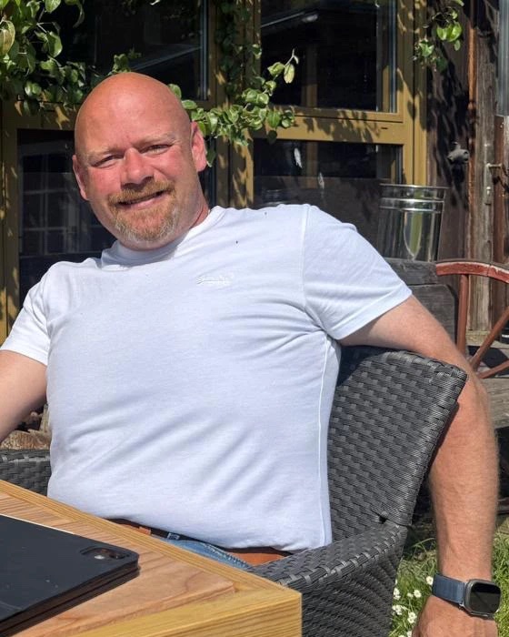 Florian Schropp, Geschäftsführer der EKRAFT GmbH, sitzt lächelnd an einem Holztisch im Freien