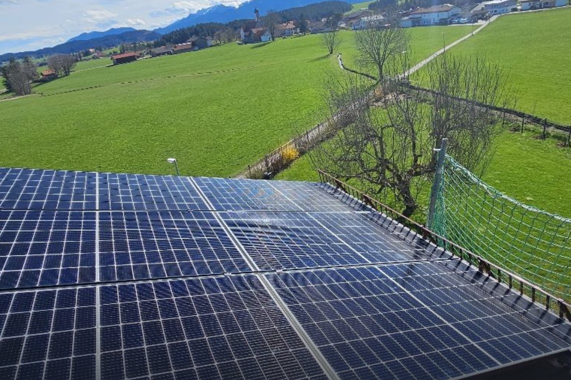 PV-Module auf einem Dach mit Blick über Wiesen in die Allgäuer Berge