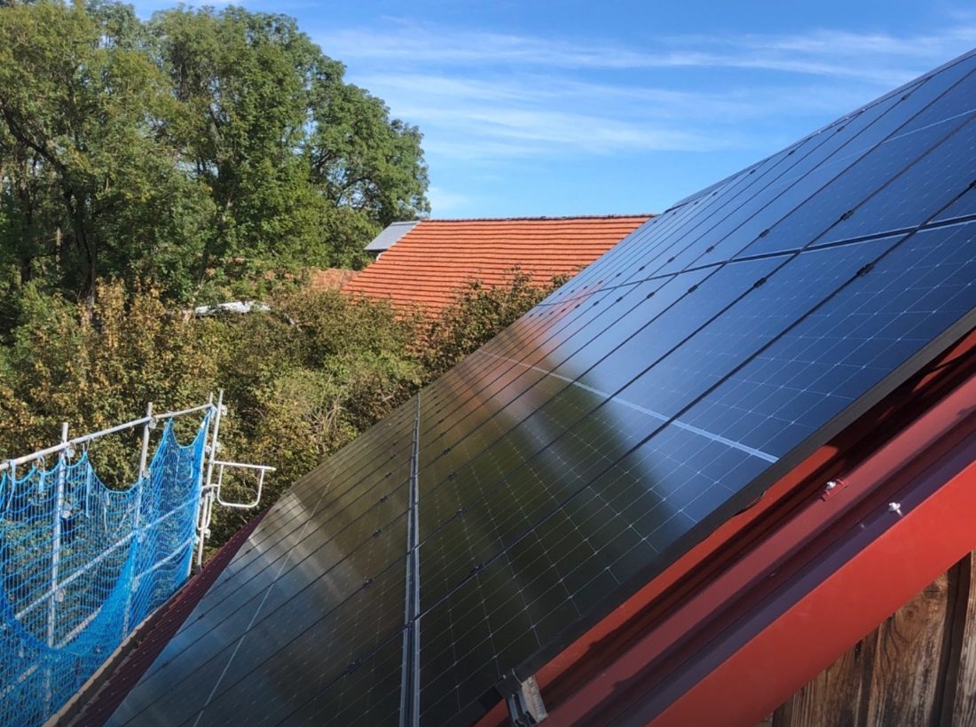 PV-Module auf einem Scheunendach mit Blick über Wiesen ins Allgäu